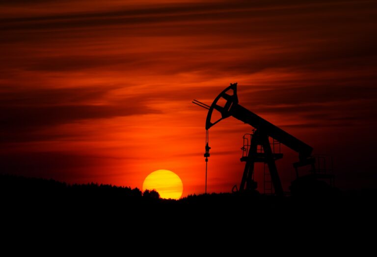 A pumpjack oil rig in front of a setting sun.